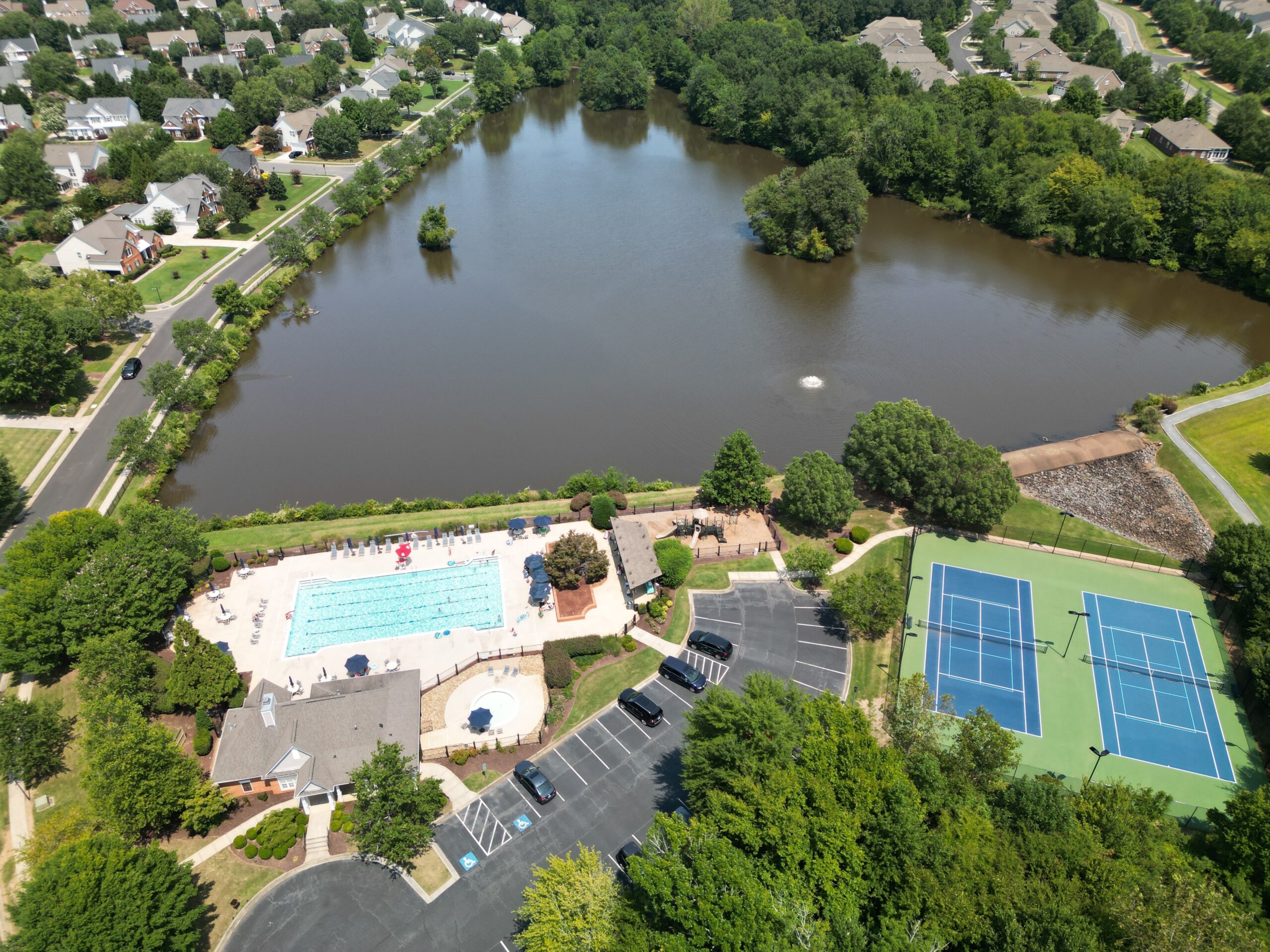 An isometric photo of a lake in the distance, with community pool and tennis courts in frame below the lake.